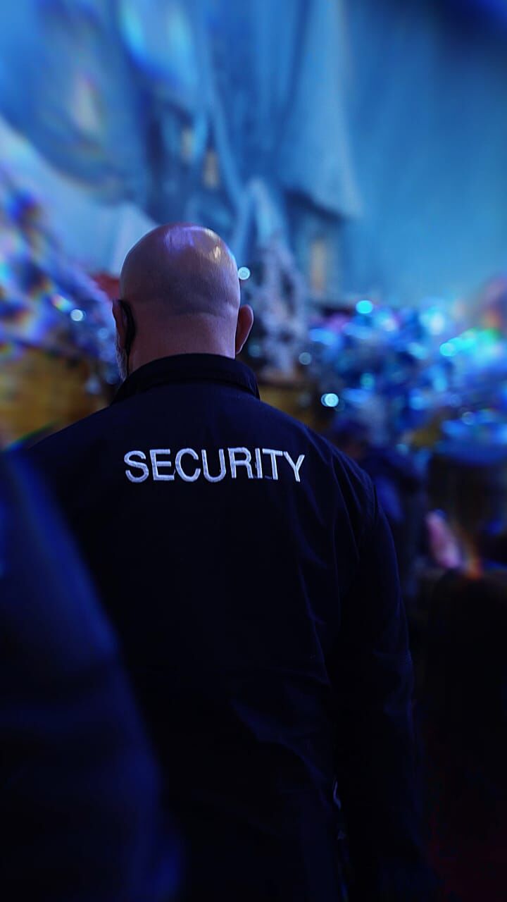 Agent in a SECURITY jacket watching a crowd under blue lights