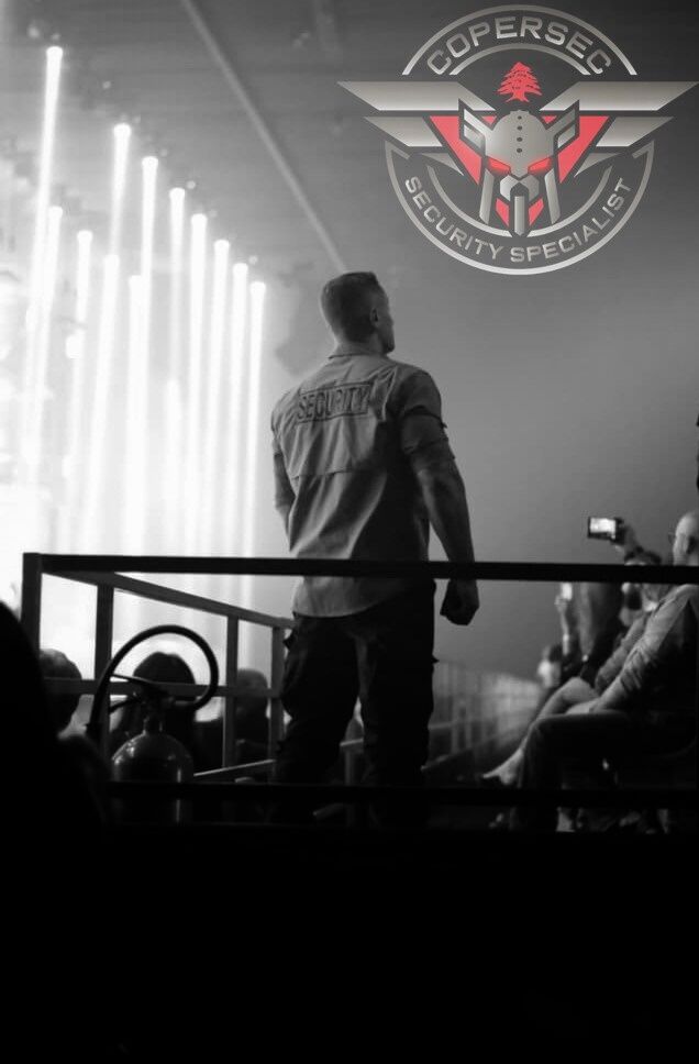 Agent watching the crowd from a stage platform, with the COPERSEC badge